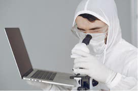 Man in suit looking through microscope, holding laptop